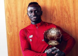 Pour l’écrivain Mabrouck Rachedi, le fait que Sadio Mané, attaquant de Liverpool, soit africain explique son déficit de reconnaissance face au Français du Real Madrid, qu’il rencontrera samedi en finale de Ligue des champions. Chronique. Le footballeur africain n’est pas assez entré dans l’histoire. Derrière ce détournement du tristement célèbre discours de Nicolas Sarkozy à Dakar en 2007, se cache une réalité : depuis toujours, les joueurs du continent font les frais d’une décote par rapport aux Européens et aux Sud-Américains. Sadio Mané en est un des exemples les plus frappants. Vainqueur de la Coupe d’Afrique des nations (CAN) avec le Sénégal, en février, deuxième du championnat anglais – le plus disputé du monde – et en finale de la Ligue des champions face au Real Madrid, samedi 28 mai au Stade de France, l’attaquant décisif de Liverpool est l’auteur d’une saison exceptionnelle. Il est donc un candidat naturel pour le Ballon d’or 2022, qui sera décerné à Paris en octobre. Oui, mais la planète football n’a d’yeux que pour Karim Benzema, le 9 fantastique de la « maison blanche » – le Real Madrid. Il est même le grand favori du trophée qui récompense le meilleur joueur du monde. Ses statistiques plaident pour le Français : « Pichichi » de la Liga (meilleur buteur avec 27 réalisations), il a guidé et porté son club jusqu’au titre de champion d’Espagne et jusqu’en finale de la Ligue des champions. Pour les observateurs, il n’y a ni débat ni doute : Benzema doit être le Ballon d’or. Pourquoi un tel écart de considération entre ces deux stars ? Au-delà des questions sportives, sa nationalité et son continent sont peut-être les véritables clés du déficit de reconnaissance de Mané. Sur la pointe des pieds En réalité, le footballeur africain est déjà entré dans l’histoire ; mais sur la pointe des pieds, presque sur un malentendu. Par une porte entrouverte en 1995, l’année où la récompense individuelle la plus prestigieuse du football mondial a été étendue aux joueurs extra-européens. George Weah, avant-centre du Paris-Saint-Germain (PSG) – et actuel président du Liberia –, avait été le lauréat. Puis plus rien, comme si le symbole suffisait une fois pour toutes. Pour rappel, lors de la saison 1994-1995, le PSG s’était classé troisième du championnat de France et s’était fait sèchement sortir en demi-finale de la Ligue des champions par le Milan AC, club que le joueur a ensuite rejoint. Cette année-là, face au Parisien, la concurrence était aussi moins brillante. Le palmarès de Weah n’a rien de comparable avec celui de Mané, dont l’armoire à trophées s’est remplie des plus prestigieuses coupes au cours des années. Parmi les triomphes de Sadio Mané, la CAN, arrachée de haute lutte face à l’Egypte de son coéquipier en club Mohamed Salah et dont il a été désigné meilleur joueur. En faisant preuve au passage d’une force de caractère remarquable, lui qui a manqué un penalty en début de match puis a inscrit celui de la victoire lors de la séance de tirs au but. De quoi lui valoir un bonus dans la course au titre de meilleur joueur du monde ? Non, car la compétition africaine ne pèse pas autant qu’un Euro ou une Copa America. Certes, on reconnaîtra que le tournoi européen est le plus dense. Mais quid du sud-américain ? Pourtant, Lionel Messi a remporté le Ballon d’or 2021 principalement grâce à la victoire de l’Argentine à la Copa. Sa saison en club avait été quelconque, individuellement et collectivement, avec des statistiques et des résultats bien en deçà de ses standards. Barcelone, son club d’alors, n’avait terminé que troisième de la Liga et avait été balayé par le PSG en huitièmes de finale de la Ligue des champions. La Coupe d’Espagne n’avait été que le lot de consolation maigrelet d’une saison en berne. La CAN ne compte pas La première CAN remportée par le Sénégal de Sadio Mané ne vaut donc pas autant qu’une Copa America conquise par Messi, voire que la Ligue des nations – compétition sans grande valeur – que Benzema a enlevée avec la France cette saison. Pis, la CAN ne compte pas. Peut-être même lui porte-t-elle préjudice puisque pendant que Mané faisait gagner son équipe nationale au Cameroun, il n’était pas sous le feu des projecteurs avec son club en Europe. Si le dribbleur sénégalais était anglais, il serait sans doute vu d’un œil plus conforme à son niveau réel. Au contraire, si Karim Benzema avait choisi la sélection algérienne, sa nationalité aurait-elle pu minorer ses performances extraordinaires ? Le fardeau de l’homme africain le leste dans la reconnaissance de son talent. Le regard qu’on porte sur lui est teinté de la condescendance avec laquelle on toise le continent. Dans le meilleur des mondes, la finale de la Ligue des champions qui oppose Karim Benzema et Sadio Mané devrait décider lequel de ces deux immenses champions soulèvera le trophée individuel le plus convoité du monde du ballon rond. Si le footballeur africain n’est pas assez entré dans l’histoire, c’est parce que d’autres ailleurs l’effacent ou l’écrivent à sa place. Mabrouck Rachedi est un écrivain franco-algérien dont la passion pour le football est née à l’âge de 6 ans lors du match Algérie-RFA de la Coupe du monde 1982. Dernier roman : Tous les mots qu’on ne s’est pas dits, éd. Grasset, le 26 janvier. Mabrouck Rachedi via Le Monde